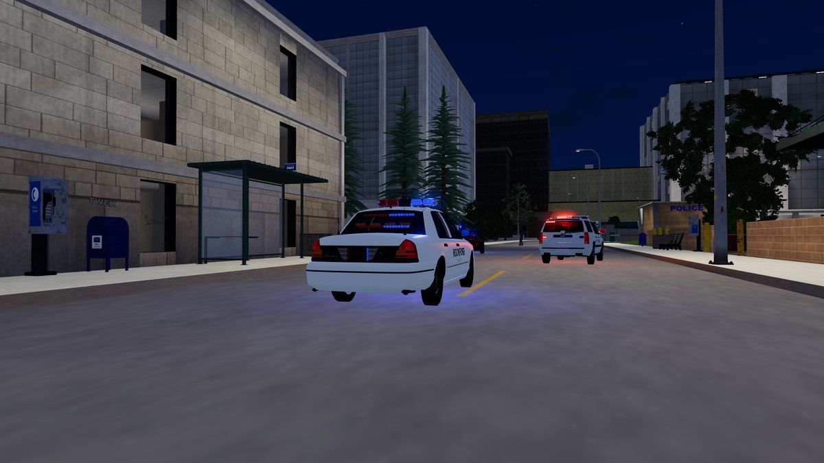 A police cruiser with its light bar on, on a lamp-lit city street at night